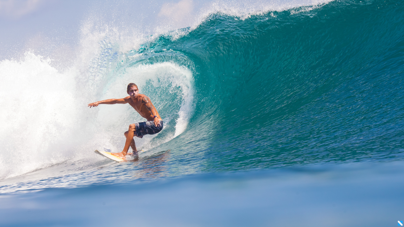Surfeur glissant sur une grande vague bleue, démontrant l'étanchéité des montres connectées adaptées aux conditions aquatiques extrêmes.
