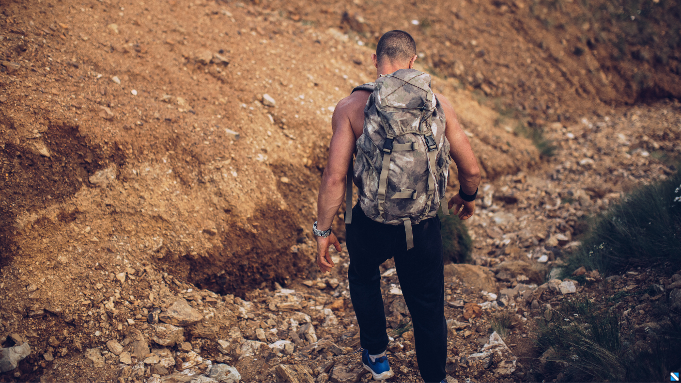 Randonneur torse nu vu de dos marchant en montagne, portant une montre GPS à son poignet gauche, illustrant la durabilité et la fonctionnalité des montres connectées en environnement extérieur.